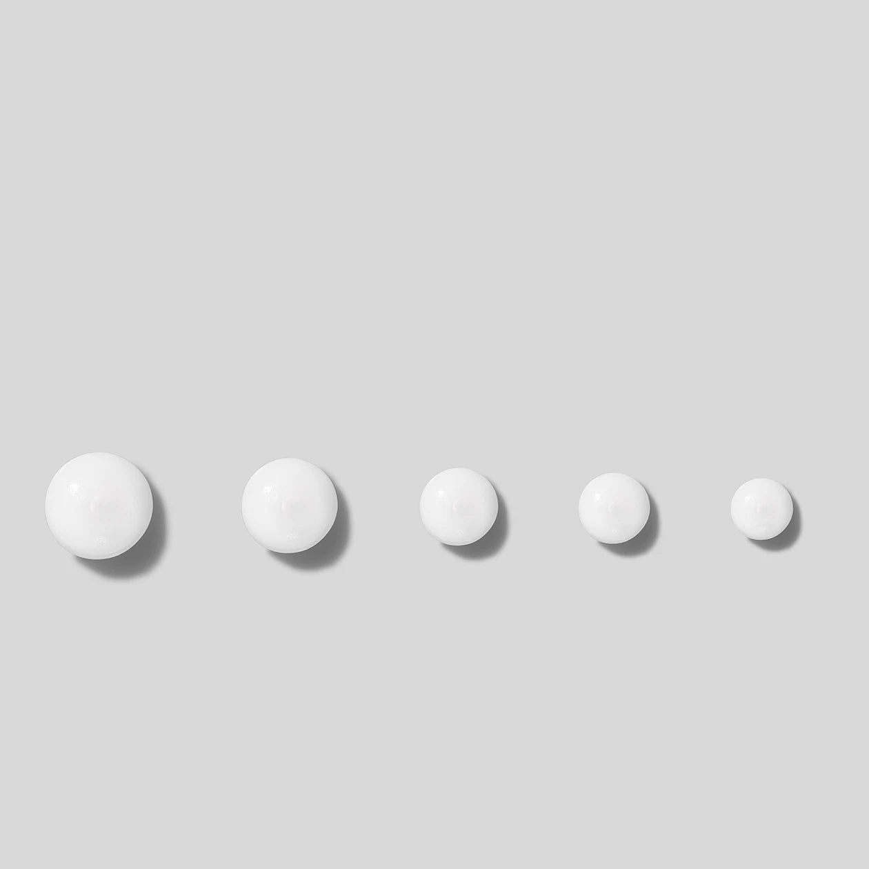 Five white drops of cream on a light gray background