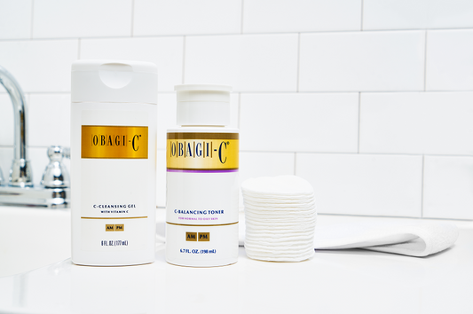 Two skincare products from Obagi-C on a bathroom counter with a tiled wall background.