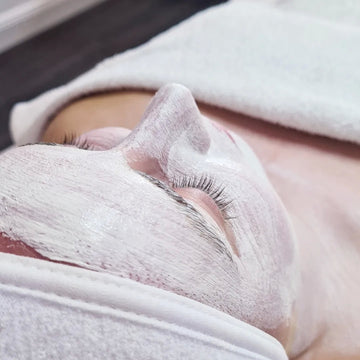 Close-up of a person receiving a facial treatment with a white towel on their face.