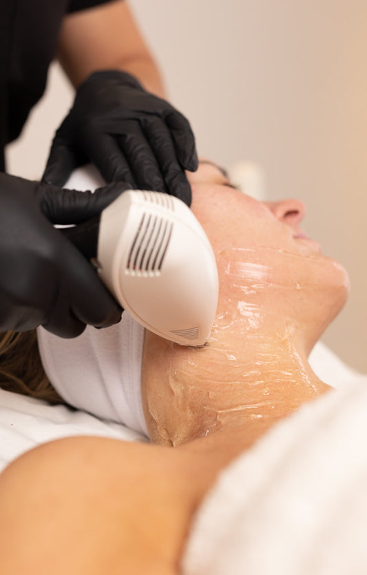 Person receiving a facial treatment with a device held by gloved hands.