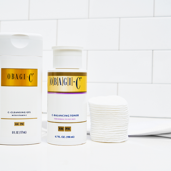 Two skincare products from Obagi-C on a bathroom counter with a tiled wall background.