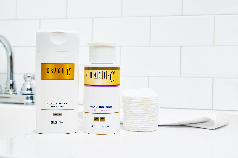 Two skincare products from Obagi-C on a bathroom counter with a tiled wall background.