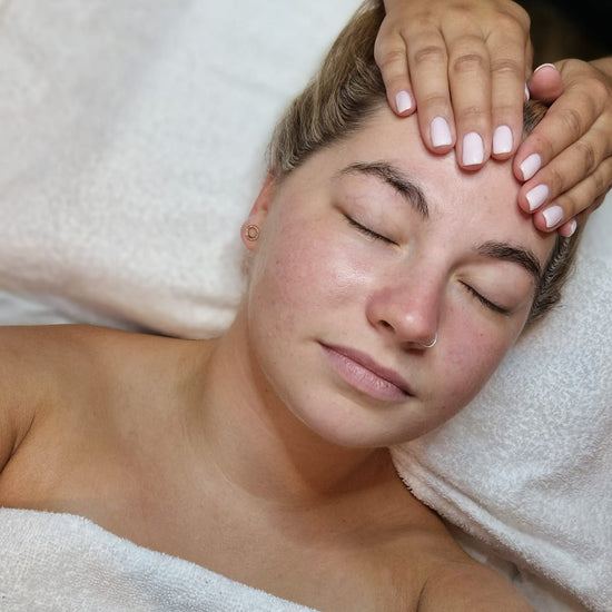 Woman receiving a facial massage with hands on her face, lying on a white towel.
