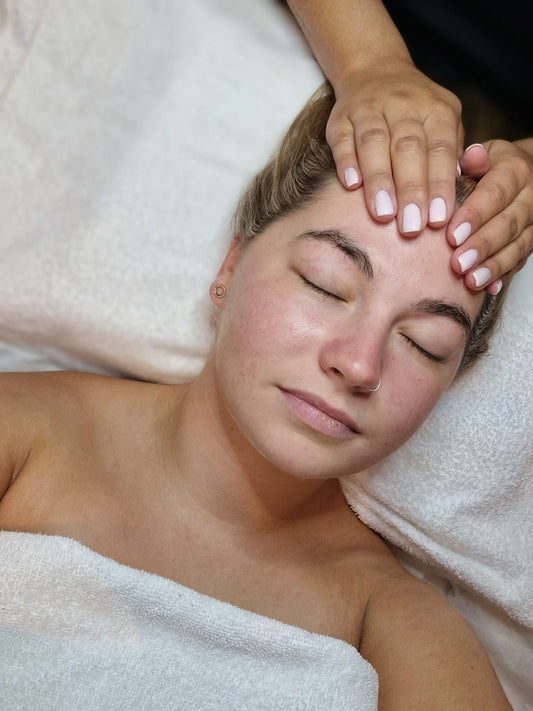 Woman receiving a facial massage with hands on her face, lying on a white towel.